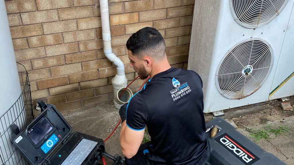 Smart Choice Plumbing plumber running a CCTV drain camera through a sewer access point